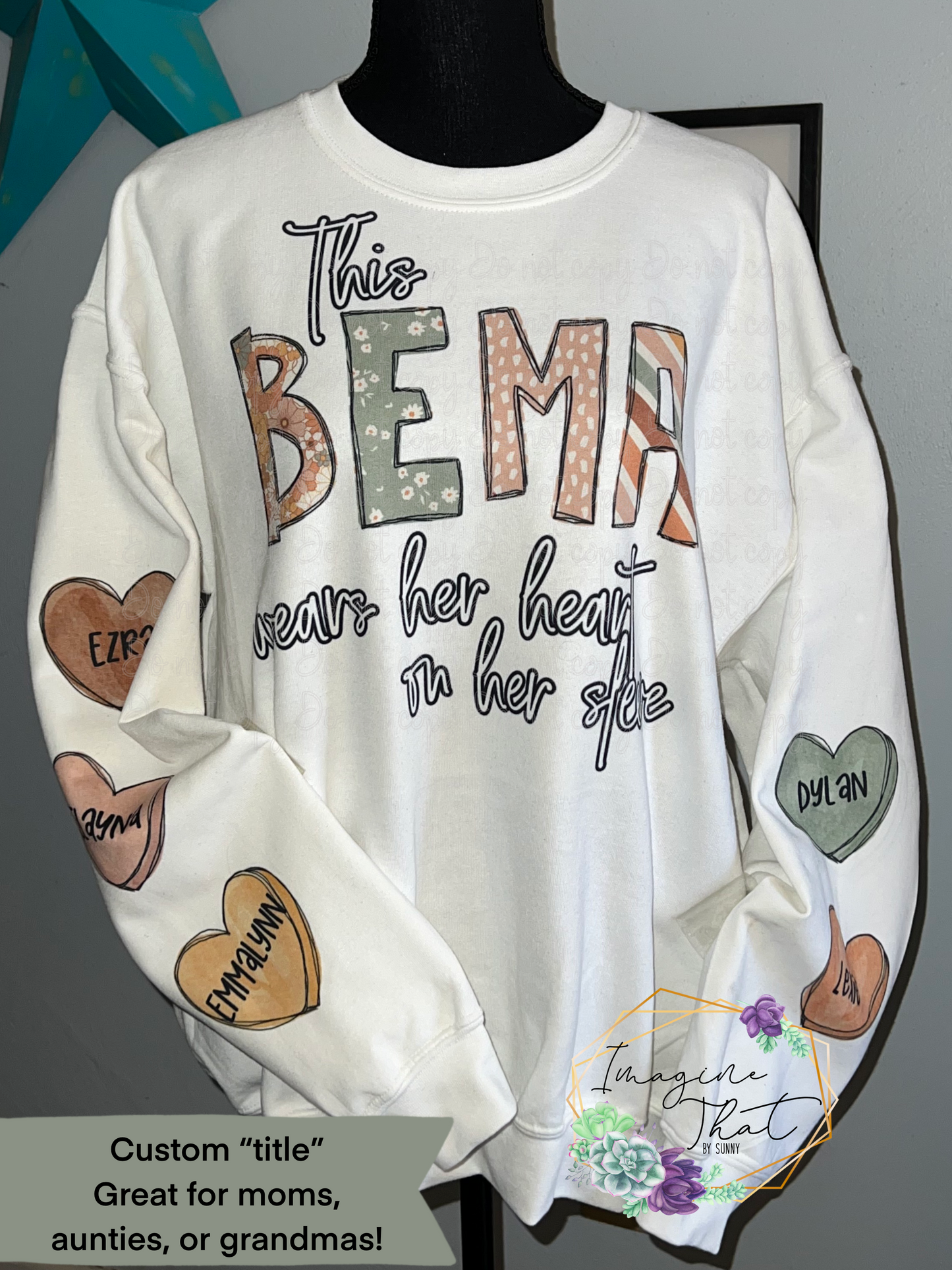 White crewneck sweatshirt with an earth tone design featuring sage green, rust, mustard, and blush tones. The shirt can have custom title such as Grandma, Mom, Nana, Lola, Mama, and more. This design says, “This Bema wears her heart on her sleeve” and had the names of her grandkids on individual hearts on the sleeves.